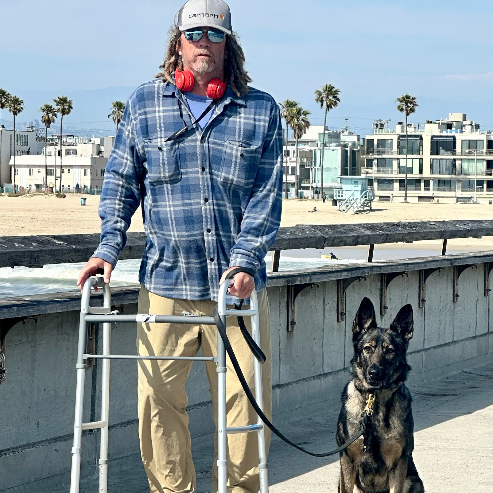 Service dog sitting next to their owner using a walker near the beach