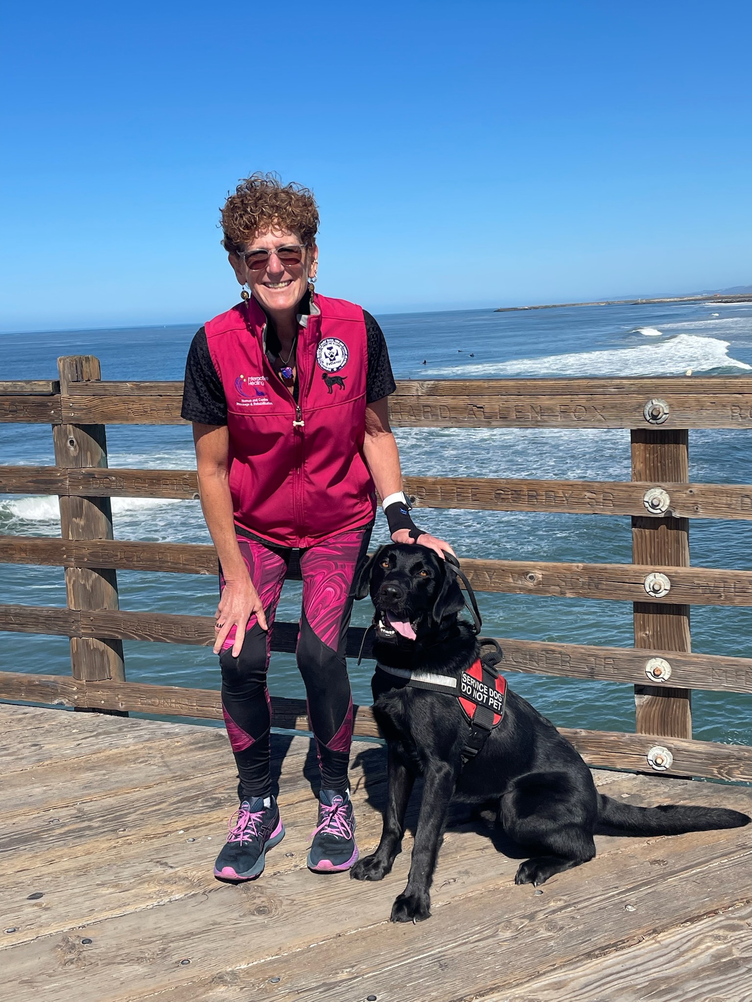 Owner and Service dog posing on a pier with the ocean behind them.